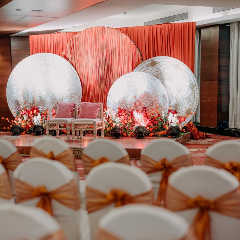 A styled wedding stage with terracotta drapes and floral mandap circles